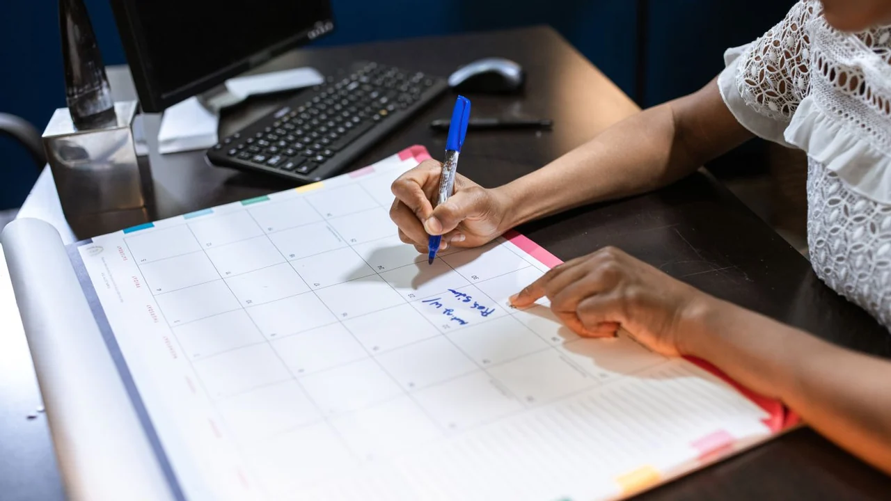 A person writing in a large monthly planner at a desk